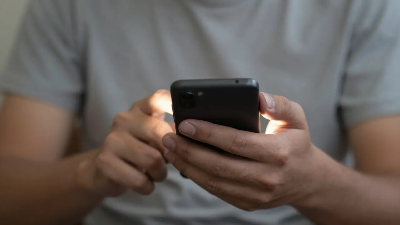 Eine Hand mit Narben und Gitarrencallus hält ein Smartphone, als würde sie einen Moment festhalten.